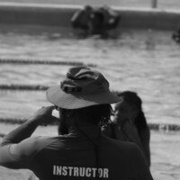 Instructor K. Palms keeps a watchful eye on swimmers during a training session at the UTech pool, ensuring safety and proper technique throughout the activity.